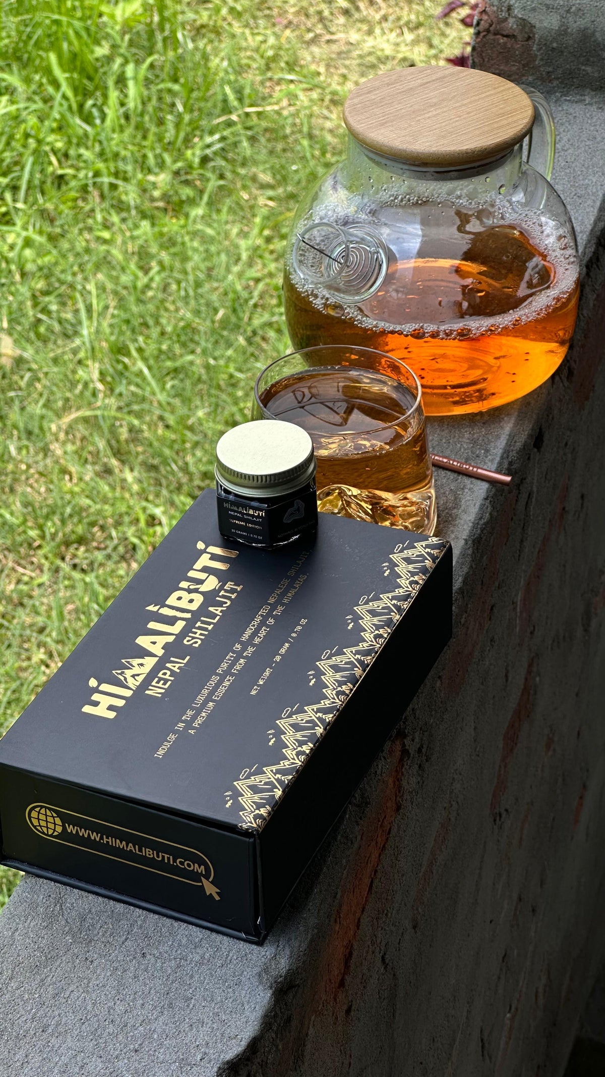 Himalibuti Nepal Shilajit resin beside a warm herbal drink in a glass cup and teapot outdoors